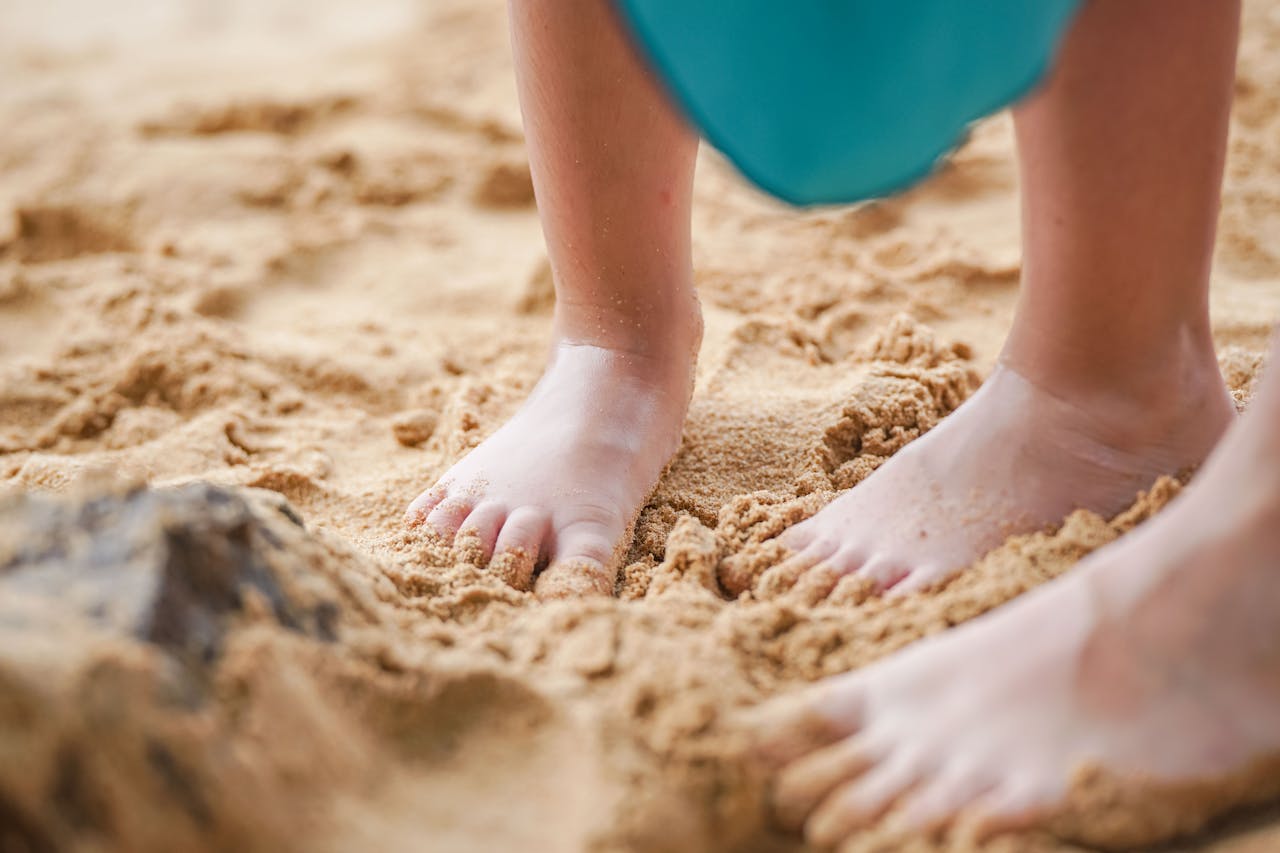 Close-up of a child's bare feet playing in sandy beach environment, conveying a sense of summer fun and freedom.